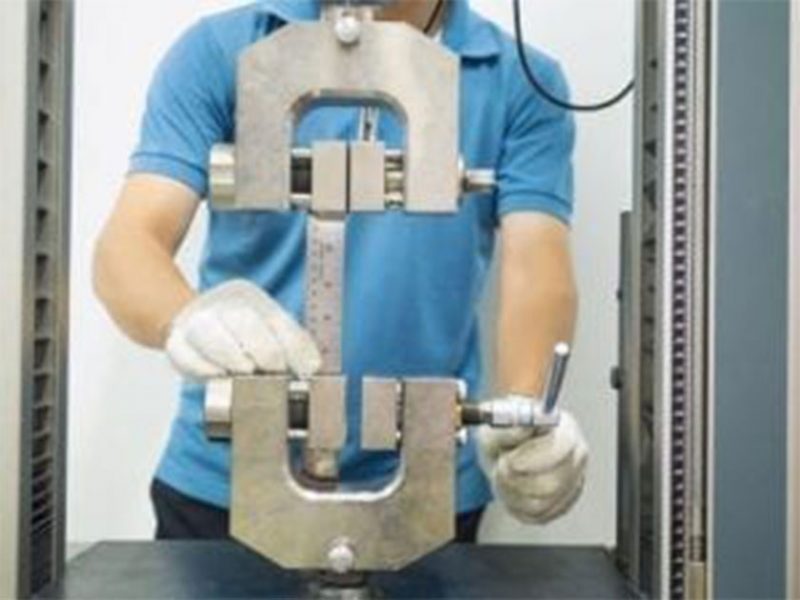 Engineer in blue shirt adjusting grips on a universal testing machine, preparing a specimen for mechanical testing.